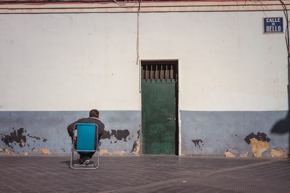 man sitting on chair facing building with closed door