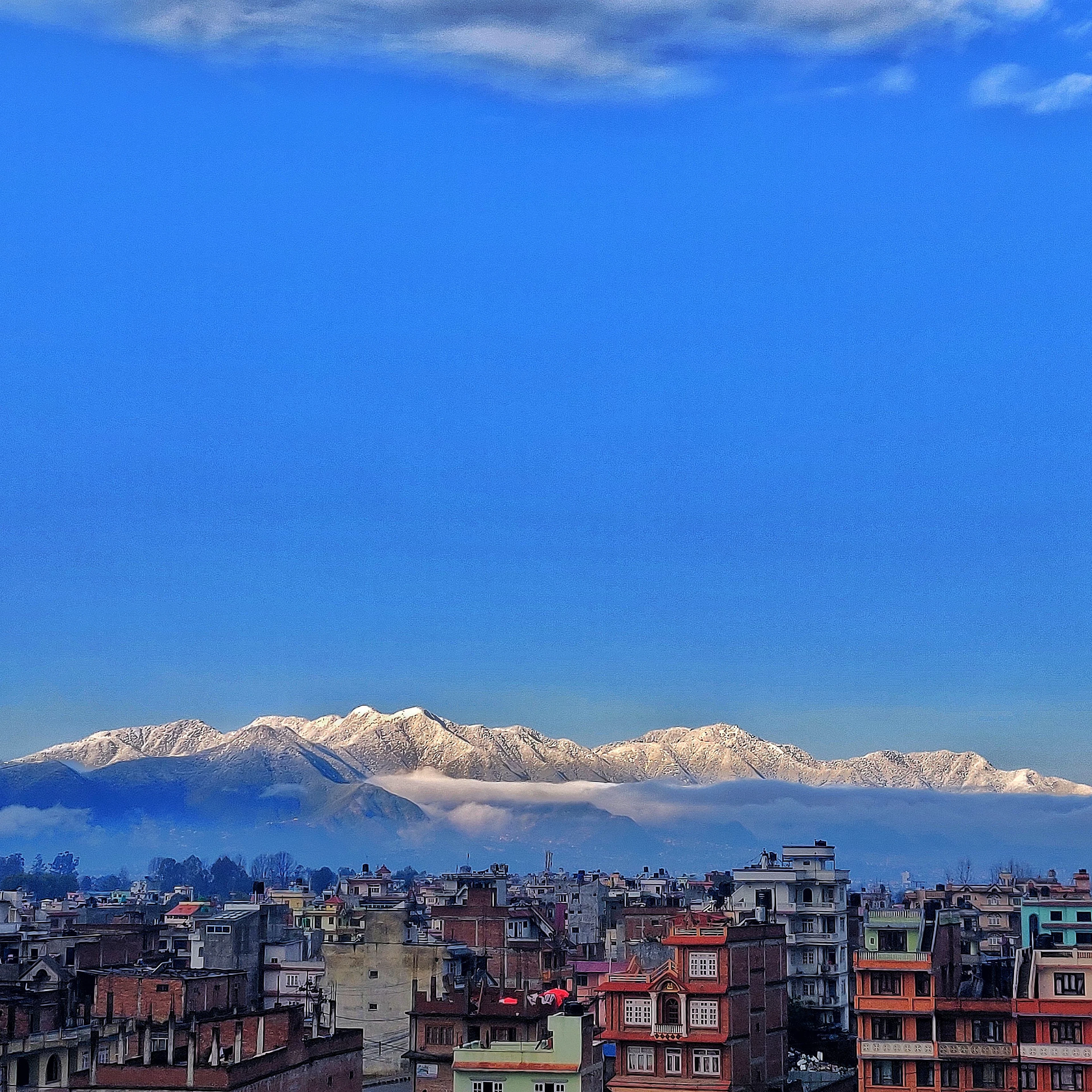 Snow-capped Himalayan peaks rise sharply above Kathmandu's dense rooftops on a clear day.