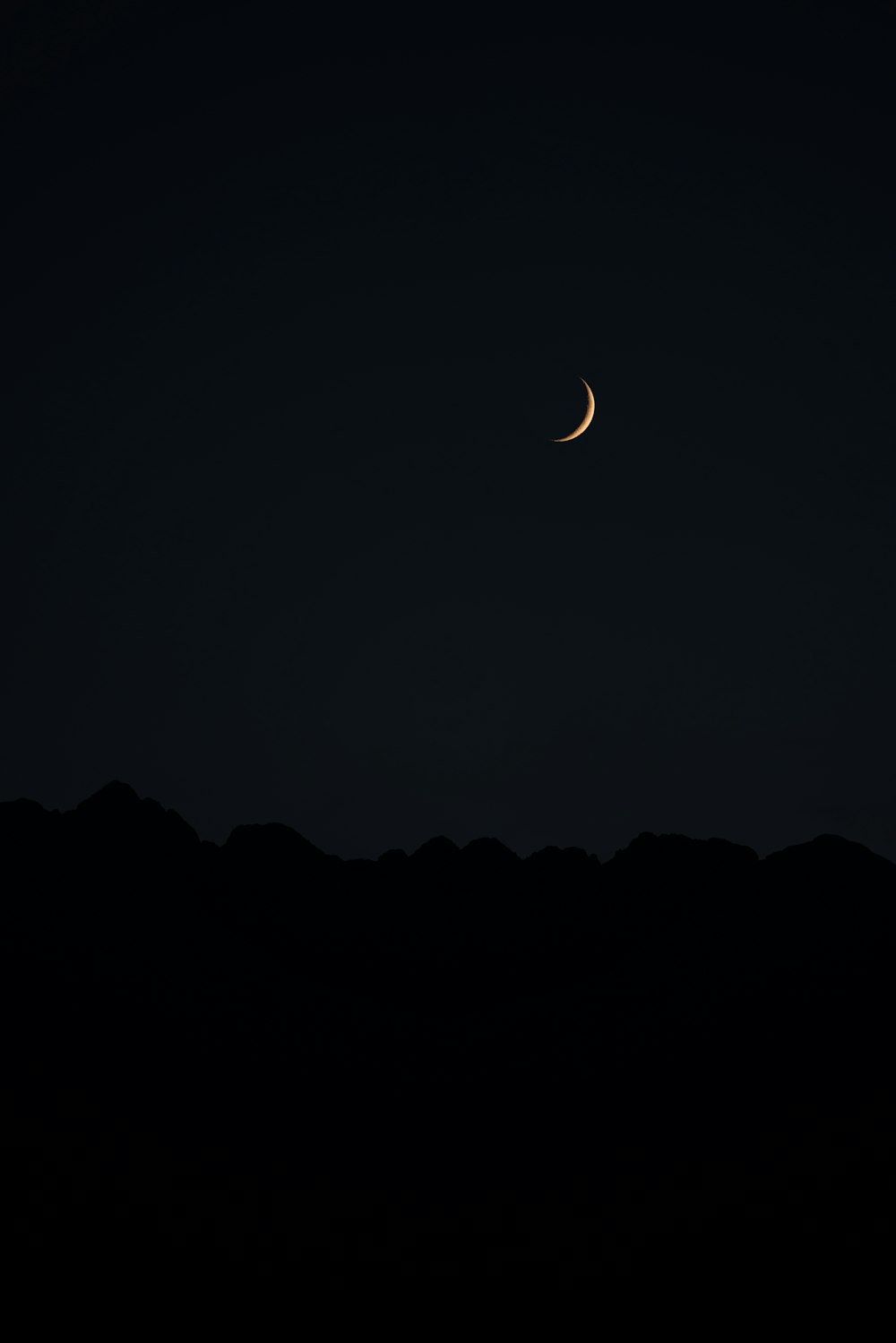 a half moon is seen in the sky above a mountain range
