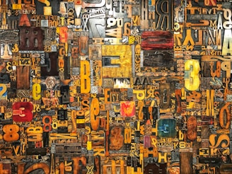 A vibrant and eclectic collage of various letters and numbers in different fonts, sizes, and colors arranged in a dense and intricate pattern. The elements appear as if they are made from different materials, including wood and metal, giving a textured and artistic feel.