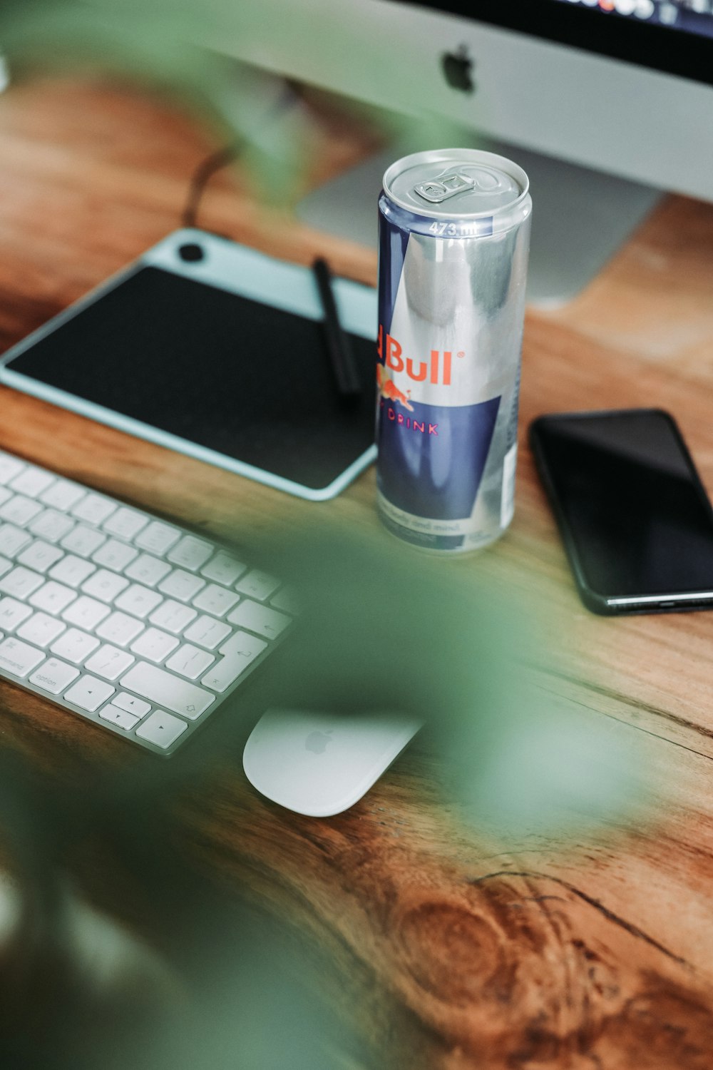 Red Bull can in between smartphone and writing pad on table