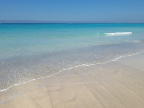 A serene beach view in Tulum with soft white sand and turquoise waters under a clear blue sky.
