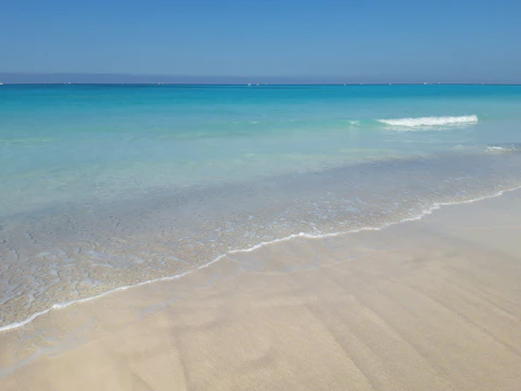 A sunlit beach with turquoise waves gently rolling onto white sand, perfect for a relaxing getaway