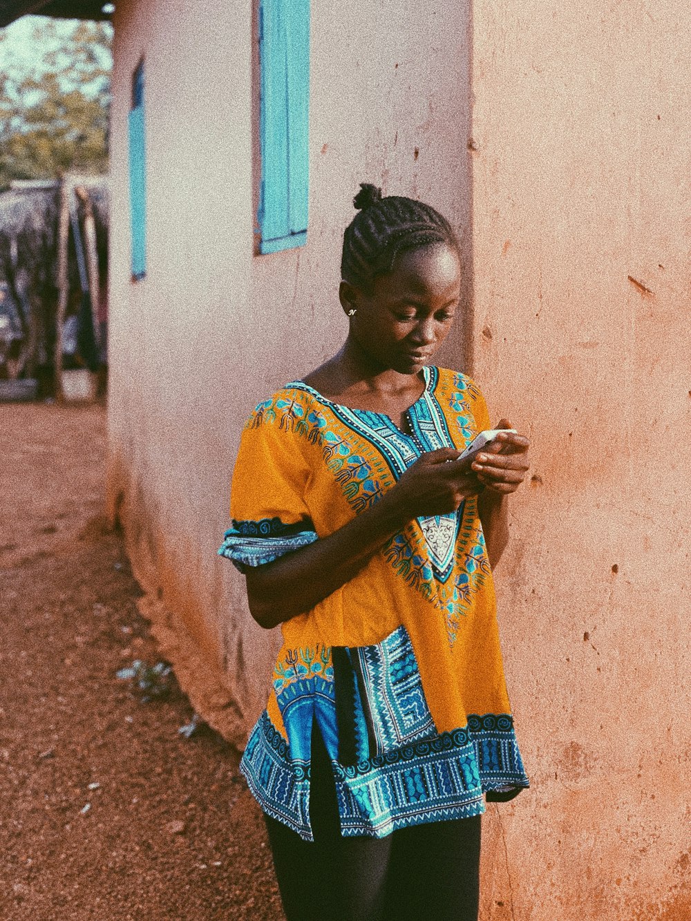 woman in orange and blue dashiki leaning on wall