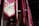 A series of vibrant red and pink fabric banners hang vertically in an indoor setting. Each banner features intricate gold and green swirling embroidery, adding a touch of elegance. The lighting is dim, with soft illumination casting shadows that enhance the rich colors and textures.