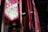 A series of vibrant red and pink fabric banners hang vertically in an indoor setting. Each banner features intricate gold and green swirling embroidery, adding a touch of elegance. The lighting is dim, with soft illumination casting shadows that enhance the rich colors and textures.