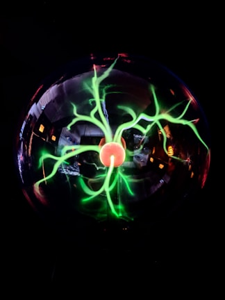 A glowing plasma globe with vibrant green and red tendrils emanating from a central core against a dark background. The tendrils appear bright and dynamic, creating an electrifying visual effect.