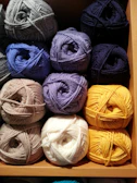 Colorful skeins of yarn arranged neatly on a wooden shelf with natural light filtering through.