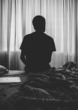 grayscale photography of man sitting on bed