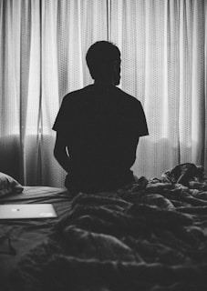 grayscale photography of man sitting on bed