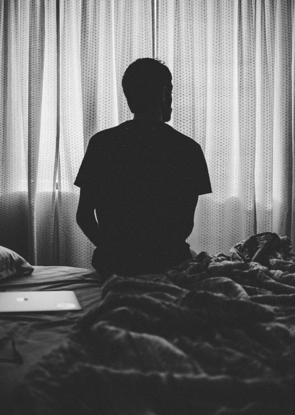 grayscale photography of man sitting on bed