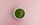 A small white bowl is filled with vibrant green powder, resting on a plain pink background.