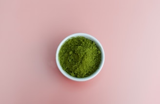 Close-up of vibrant green moringa leaves with powder in a rustic bowl on a wooden table.