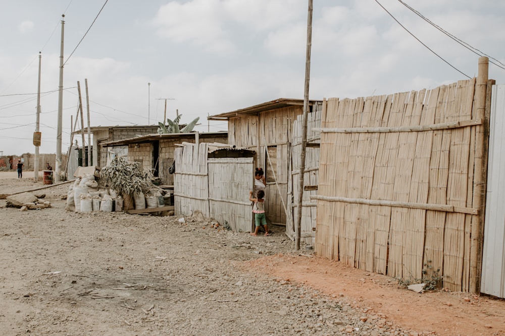 a boy standing outside of a shack next to a fence