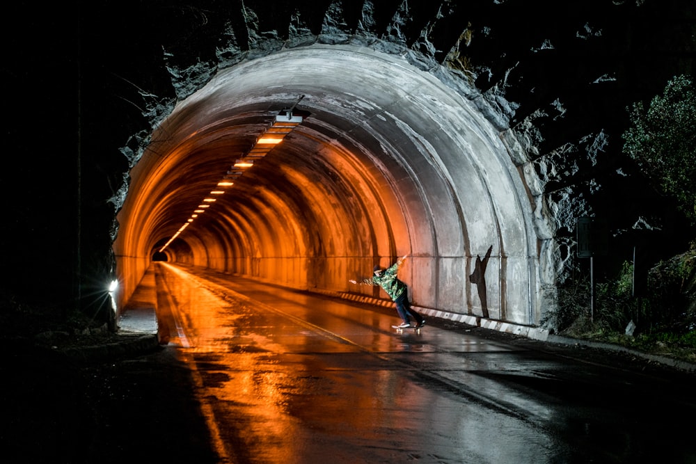 photography of man playing skateboard inside tunnel