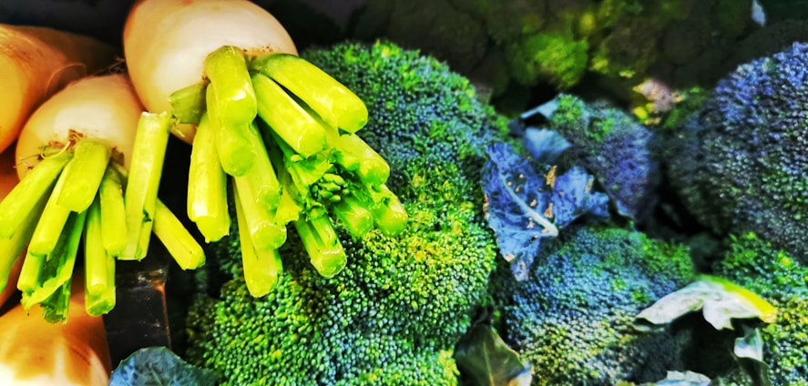 A close-up of fresh green broccoli heads and white radishes with their green stems, displaying a vibrant and healthy appearance.