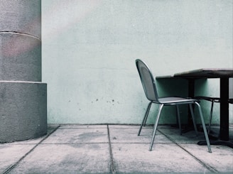 An aluminum outdoor dining chair with a minimalist design, placed on a sunlit patio surrounded by greenery.