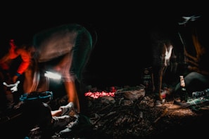 A hand holding a flask beside a campfire under a starry night sky.