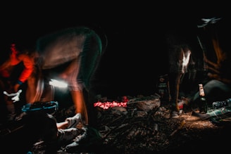 A hand holding a flask beside a campfire under a starry night sky.