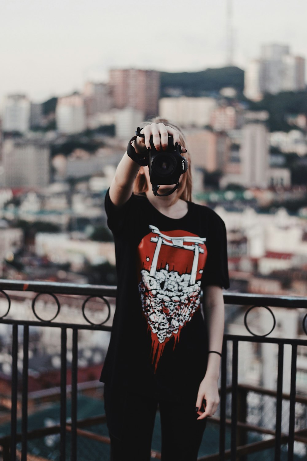 woman standing and covering her face with camera beside railing