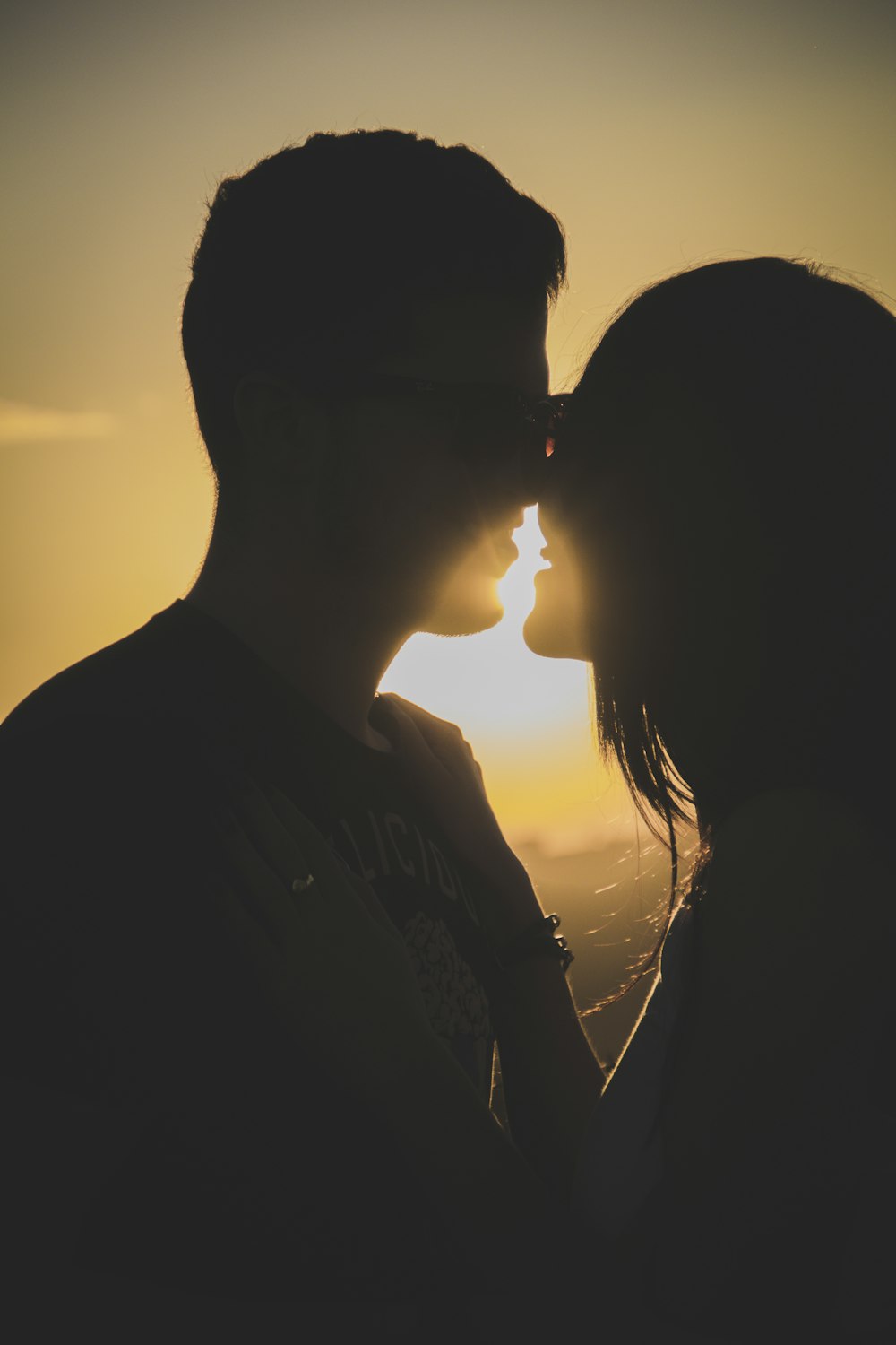a man and a woman kissing in front of the sun