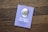 A book titled 'The Tale of Peter Rabbit' by Beatrix Potter is placed on a wooden surface. The cover is a light purple color featuring an illustration of a rabbit in a blue jacket. The text on the cover is positioned below the illustration.