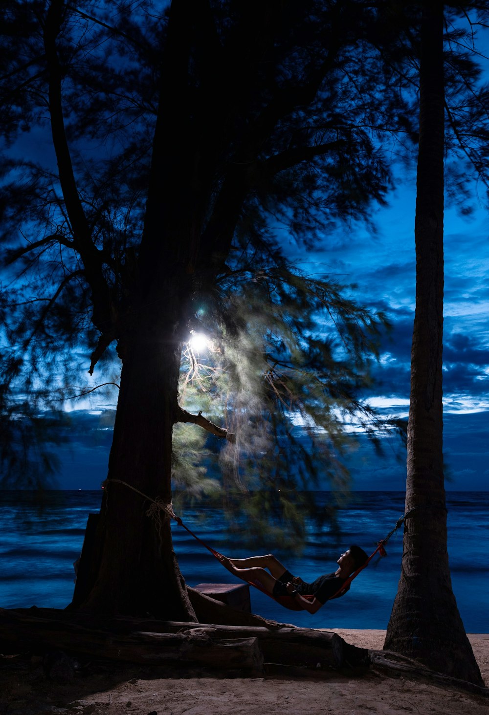 夜間の海岸近くのハンモックに座る男性