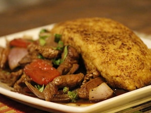 A plate of food featuring a golden, crispy fried item on the right side and a savory stir-fry mixture on the left, including pieces of beef, tomatoes, onions, and herbs.