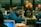 A group of people are working together in a collaborative environment. They are focused on their laptops, possibly engaged in a workshop or coding session. The room is softly lit with warm tones, and a few orange balloons are visible in the background.