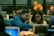 A group of people are working together in a collaborative environment. They are focused on their laptops, possibly engaged in a workshop or coding session. The room is softly lit with warm tones, and a few orange balloons are visible in the background.