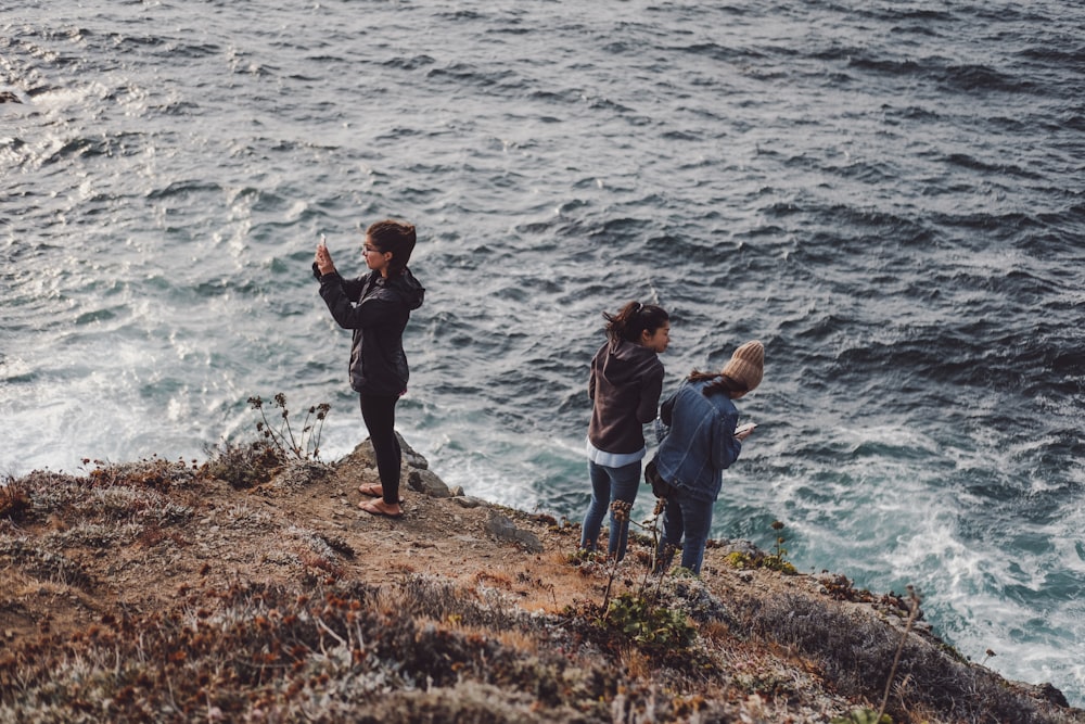 three girls standing on ground near body of water