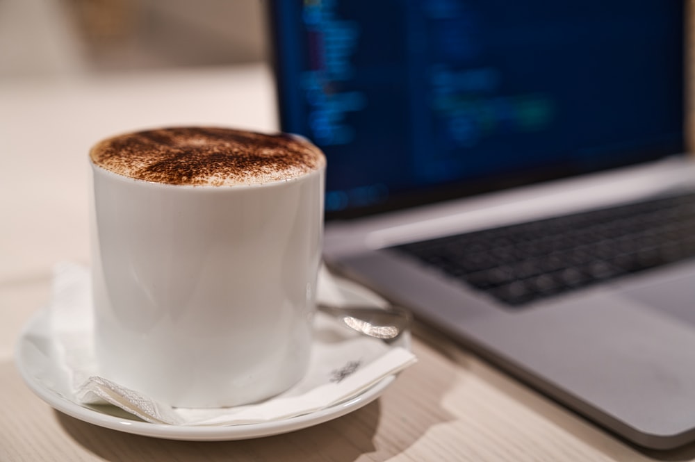 Cappuccino en taza en platillo al lado de la computadora portátil