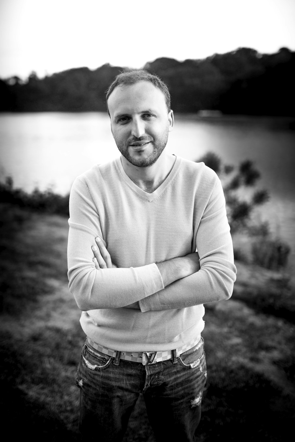 man smiling and standing crossing his arms in front of body of water