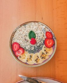 smoothie oatmeal topped with sliced of bananas and strawberries