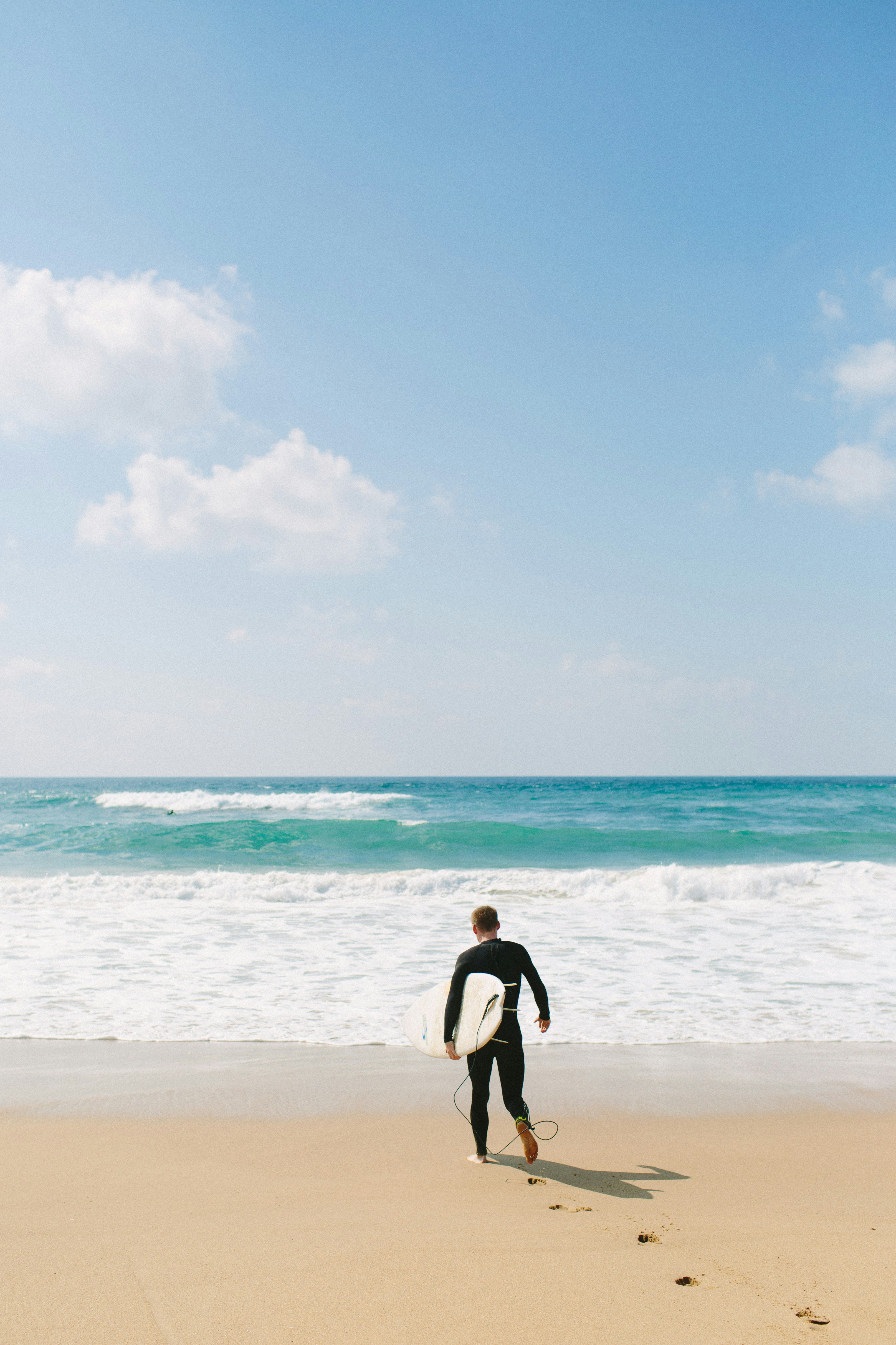 man carries surfboard towards shore