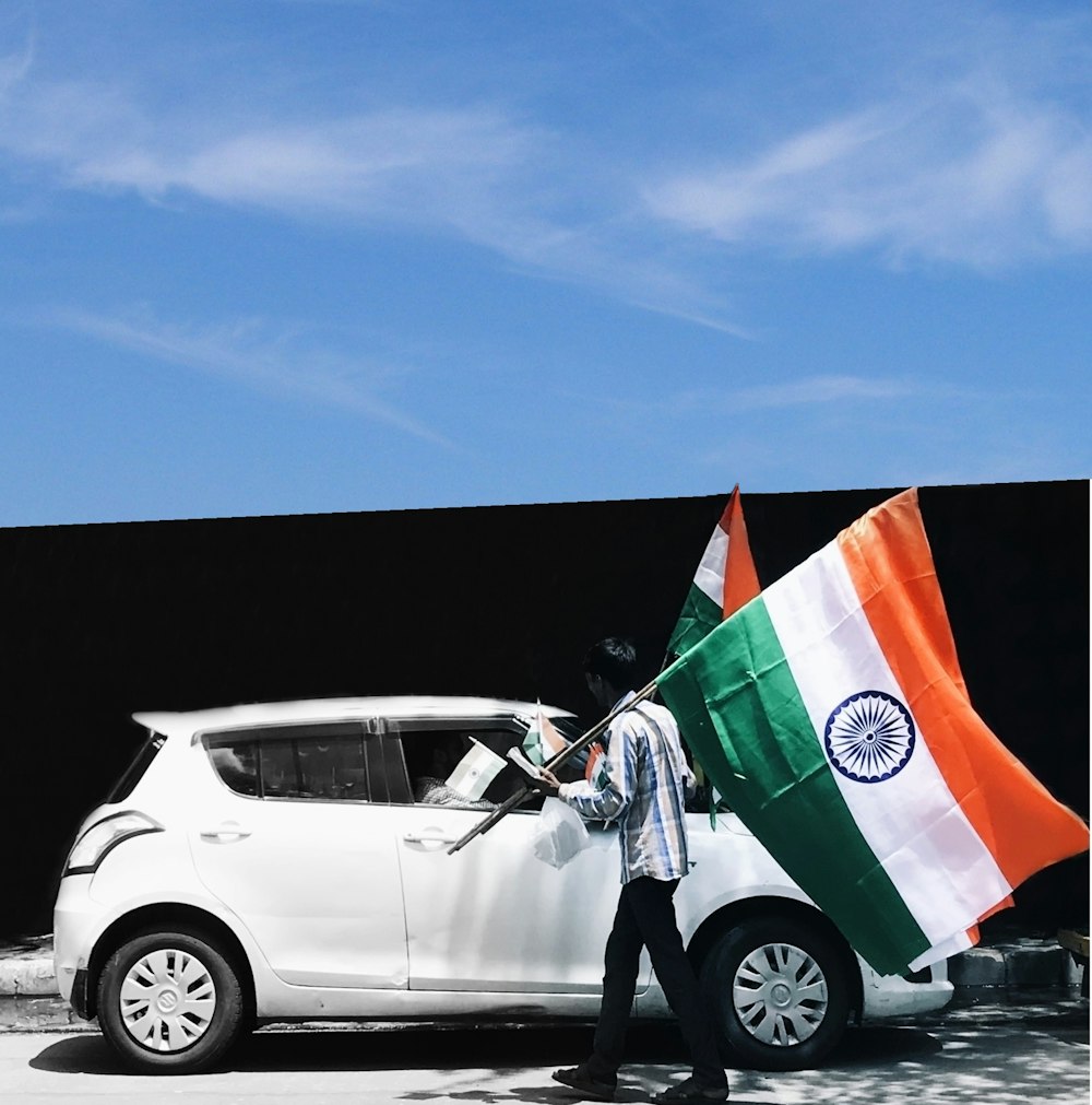 hombre sosteniendo la bandera de la India al lado de un coche blanco