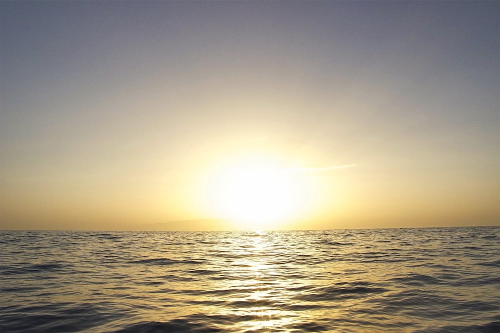 body of water under white sky at golden hour