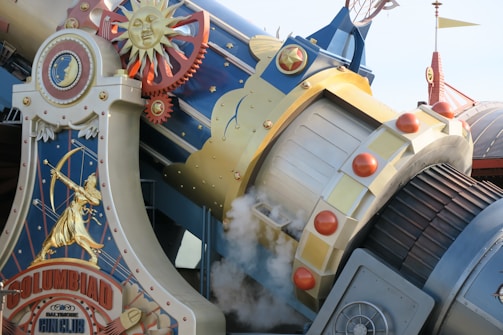 The image features a steampunk-inspired structure with intricate gears, celestial motifs, and decorative golden accents. It includes a large mechanical component resembling a cannon, with smoke emerging from its opening. A sun motif with a smiling face and an archer are depicted prominently on the surface, suggesting a blend of industrial and cosmic themes.