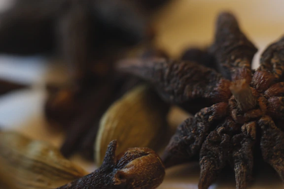 A vibrant close-up of fresh cardamom pods and peppercorns spilling from a rustic wooden bowl.