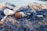 A sandy beach is littered with various types of plastic waste and blue fishing nets. Items such as plastic bottles, caps, and straws are entangled in the netting, highlighting pollution and environmental concerns.