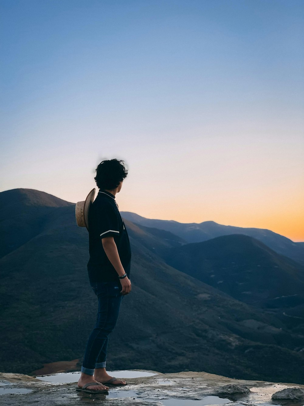 man standing on rocky hill facing mountain