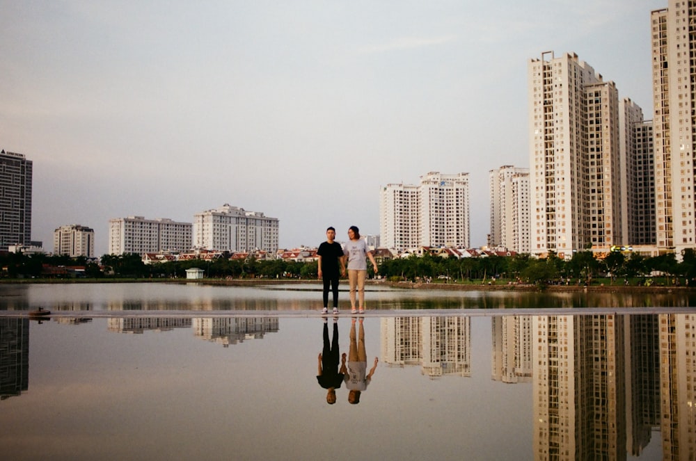 two person standing beside body of water near buildings during daytime