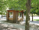 Wooden kiosk nestled among lush green trees near the Varzi public pool on a sunny day