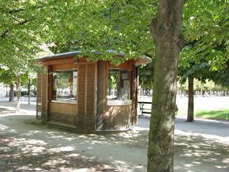 A wooden kiosk nestled among lush green trees beside a sparkling community pool on a sunny summer day.