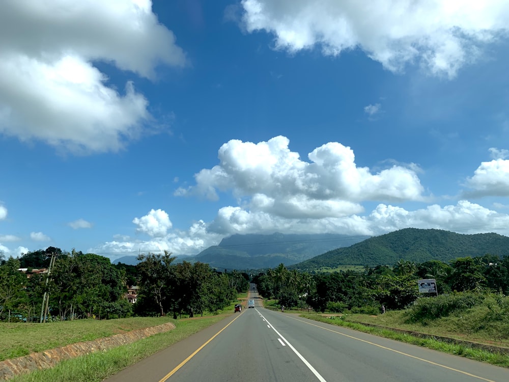 road between green trees near mountain at daytime