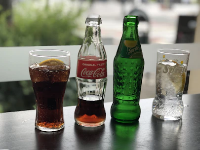 Refreshing soda cans and colorful fruit juices on a wooden table with ice cubes.