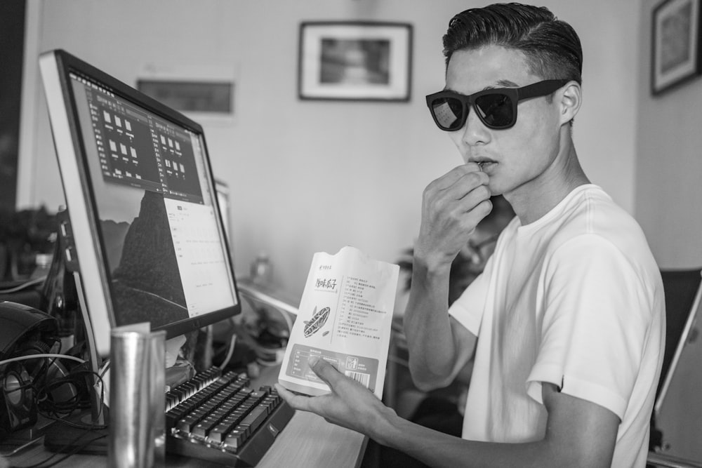 grayscale photo of man wearing crew-neck shirt wearing sunglasses using computer