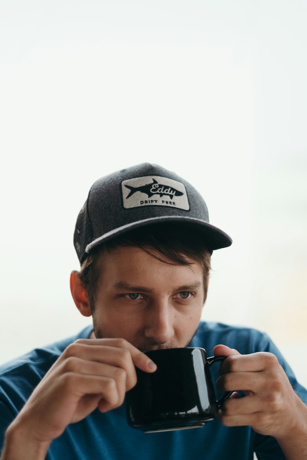 man wearing gray and white cap holding black ceramic mug