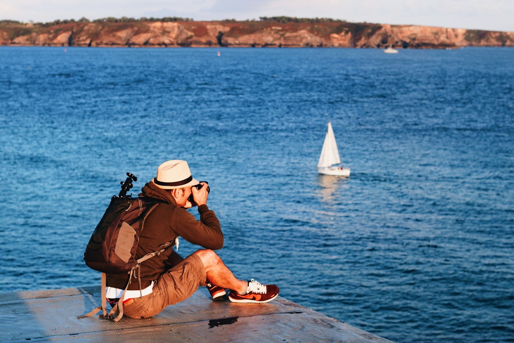 uomo seduto sul molo che scatta foto del mare