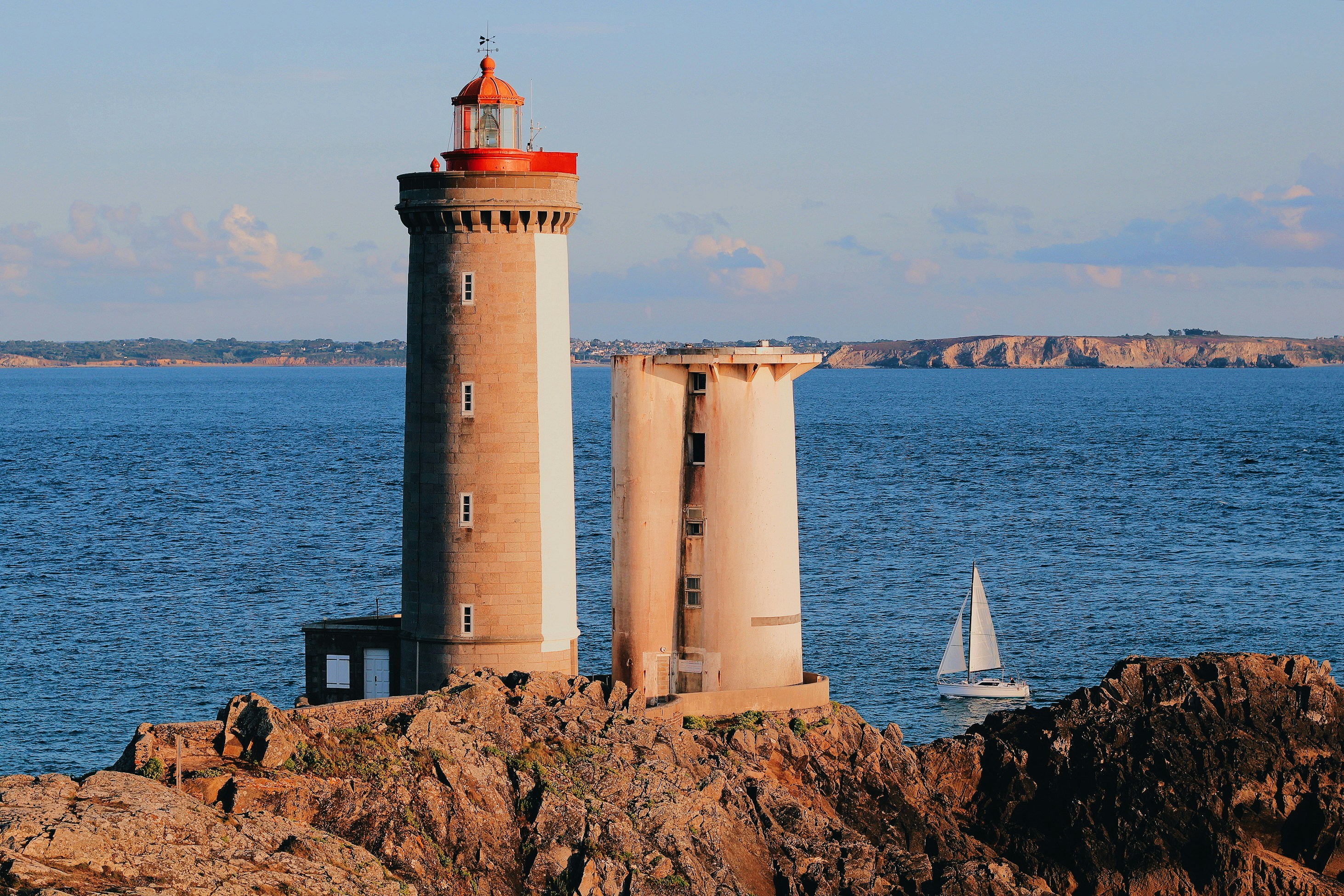 brown and white lighthouse across white sailboatby Marin Tulard